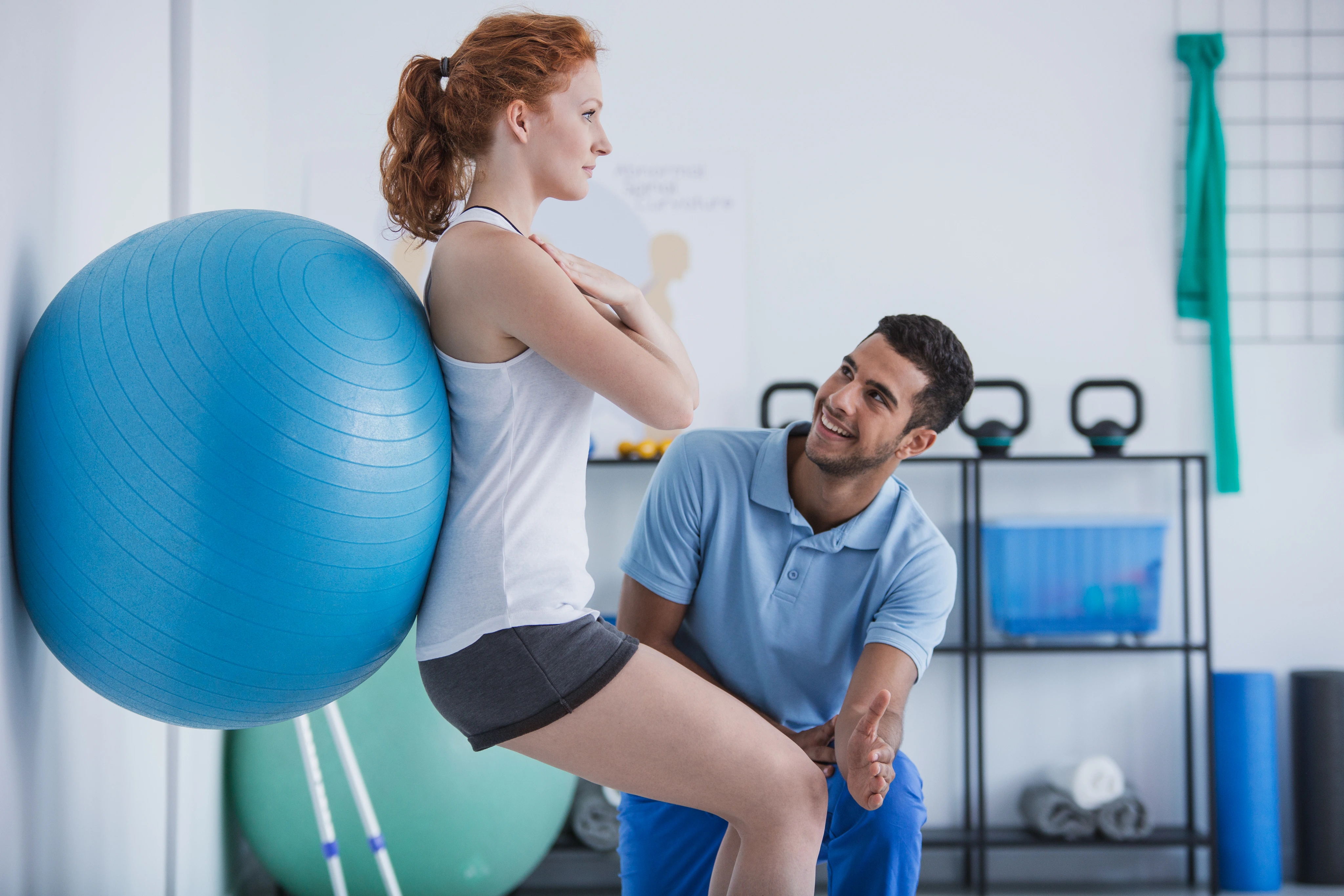 A physical therapist guiding a patient through an exercise-ball squat